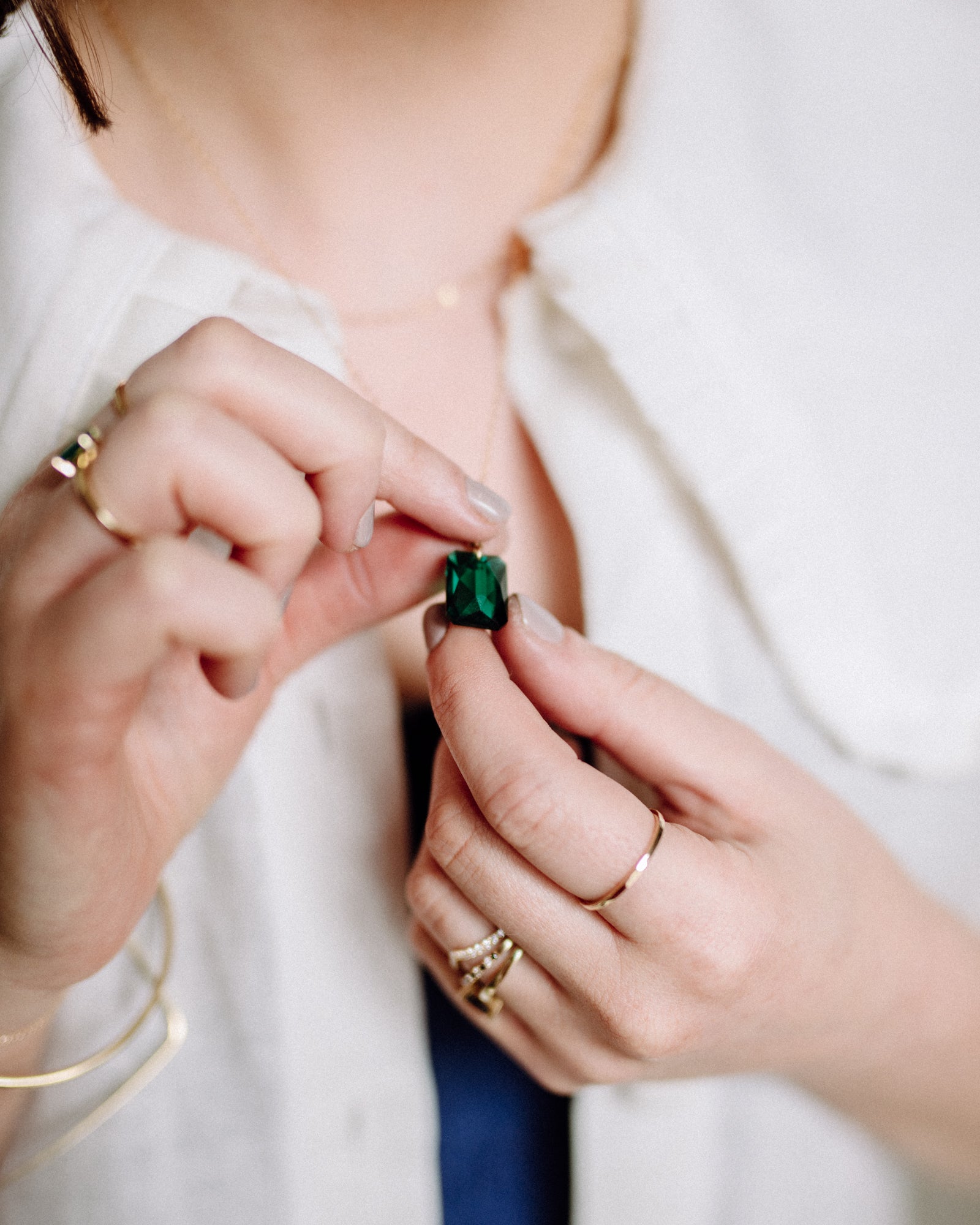 Two hands hold an emerald cut emerald green Swarovski crystal pendant on a gold chain by MoMuse