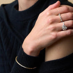 Woman wearing a dark sweater, diamond rings and a gold bracelet against a beige background