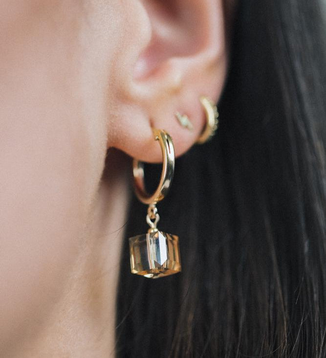 A person wearing gold filled cube clip hoop earrings with a crystal cube dangle.