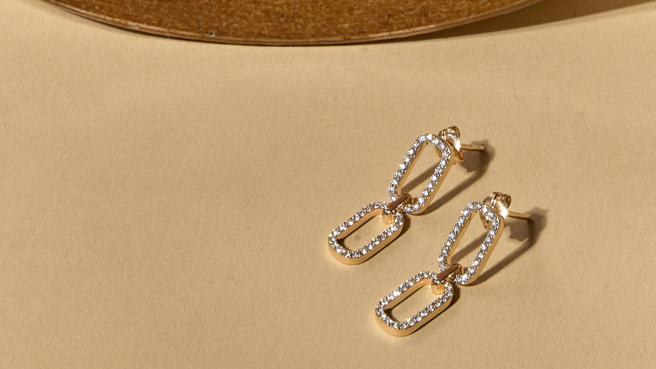 Pair of gold chain-style earrings on a beige surface
