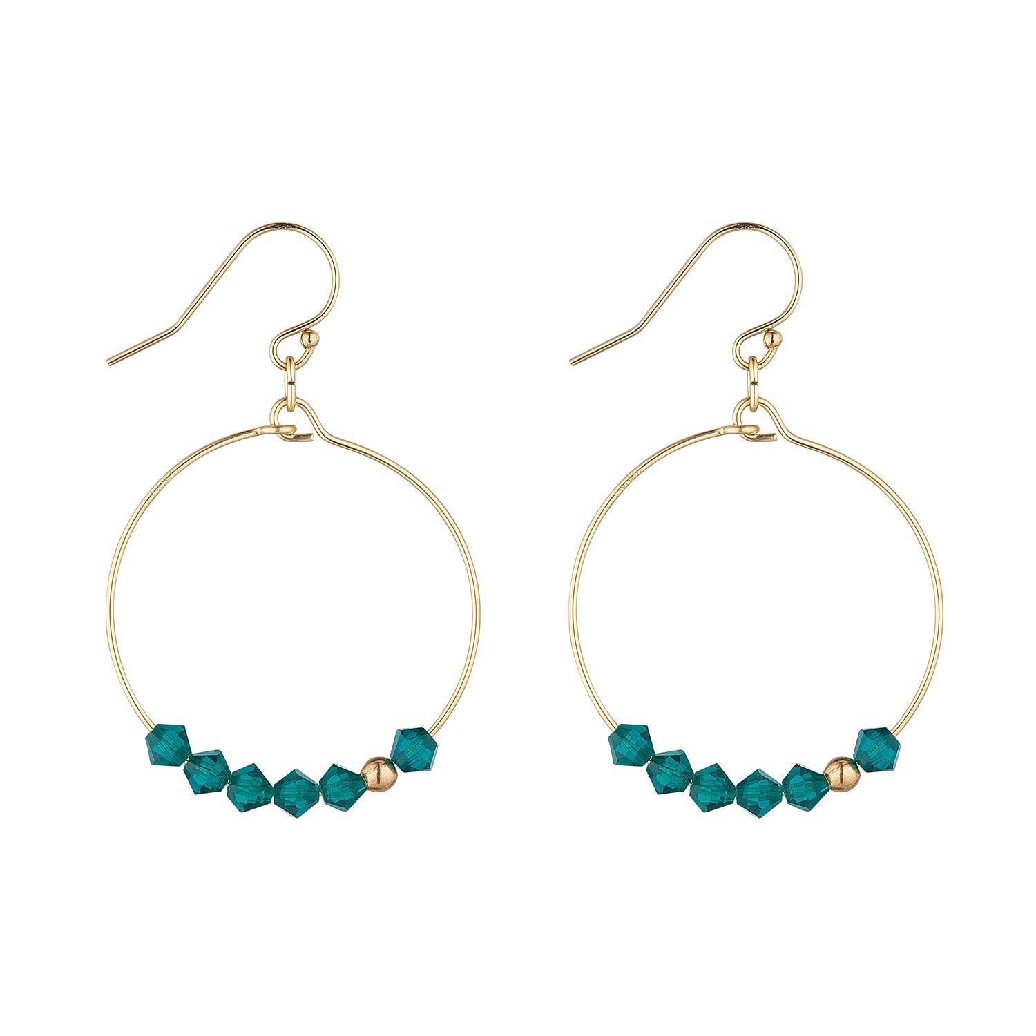 A pair of gold-filled hoop earrings featuring a sparkling row of green crystals, with a single asymmetrical gold-filled bead at the top.