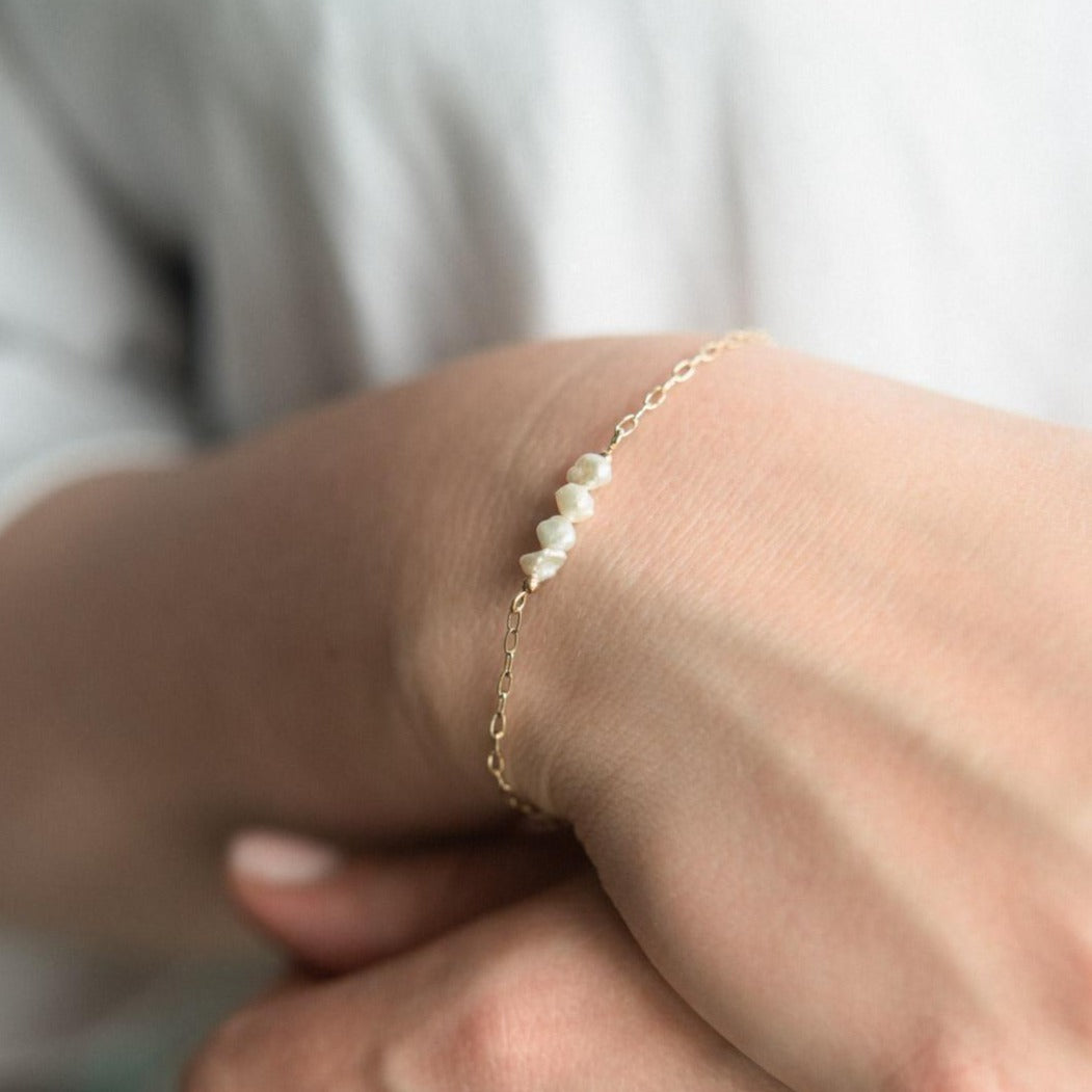 A gold filled bracelet with small saucer pearls on their wrist.